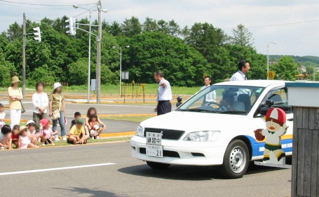 教習車と指導員を前に交通安全教室を受ける子どもたち