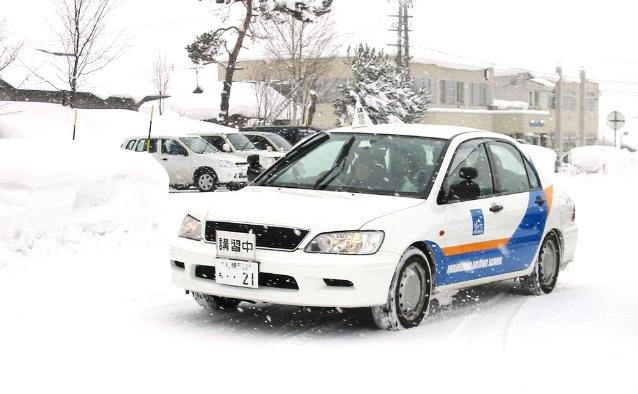 冬の教習所で、積雪のある道路を運転練習中の教習車
