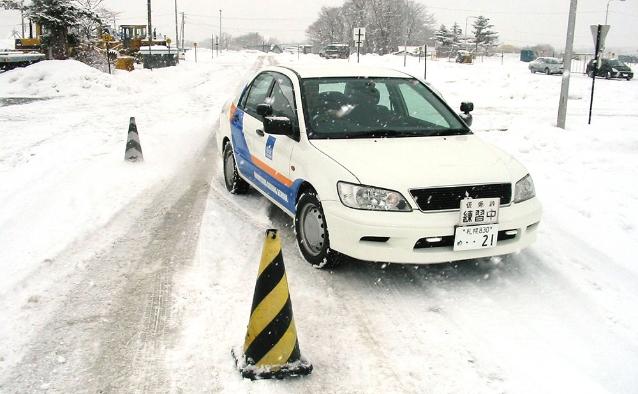 雪道に設置されたコーンの間を走行する教習車。